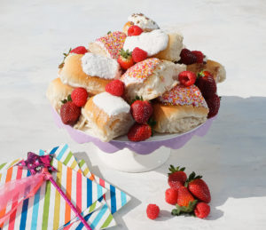 Finger Buns cut in half on on a cake stand with fruit